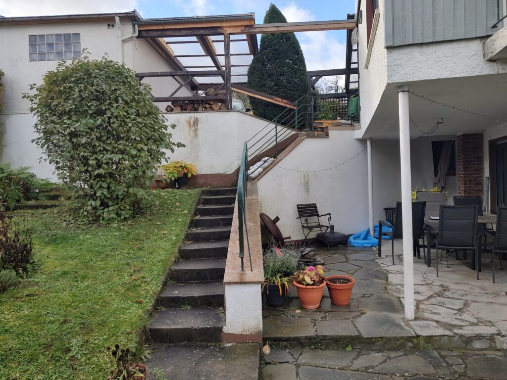 Gepflegter Garten mit Rasen, Strauch und Außentreppe an einem Wohnhaus