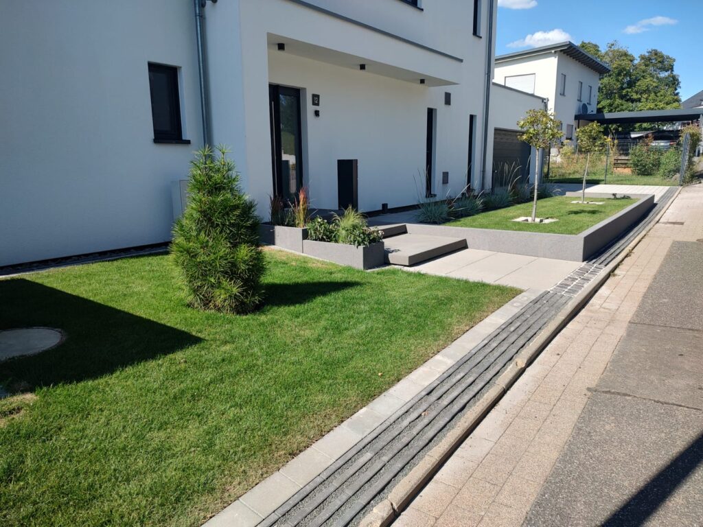 Rasenfläche mit Pflasterstreifen und Entwässerungsrinne vor einem Neubau