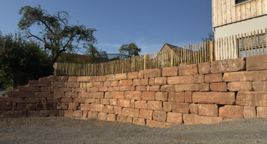 Trockenmauer aus großen Sandsteinblöcken mit Holzzaun